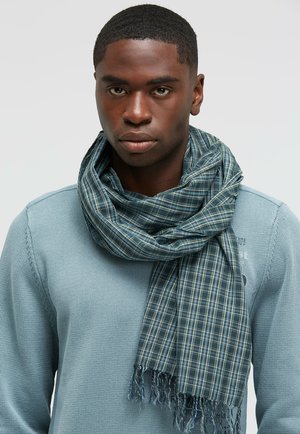 Blaues Karoschäfchen aus leichtem Stoff, mit fransigen Enden und einer weichen Textur, um den Hals eines Modells gewickelt.
