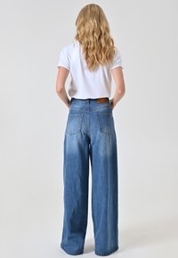 Wijde blauwe denimbroek met een vervaagd effect, hoge taille en twee achterzakken, gecombineerd met een effen witte T-shirt.
