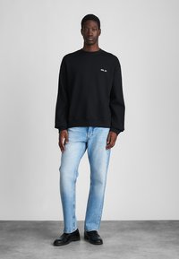 Sweatshirt noir avec un col rond et un texte brodé. Jeans bleu clair avec une coupe décontractée. Des chaussures noires complètent l'ensemble.
