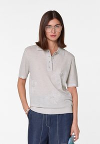 Beige polo shirt met korte mouwen van lichte stof, voorzien van bloemenborduursel op de voorkant en een drie-knopenpok met een relaxte pasvorm.