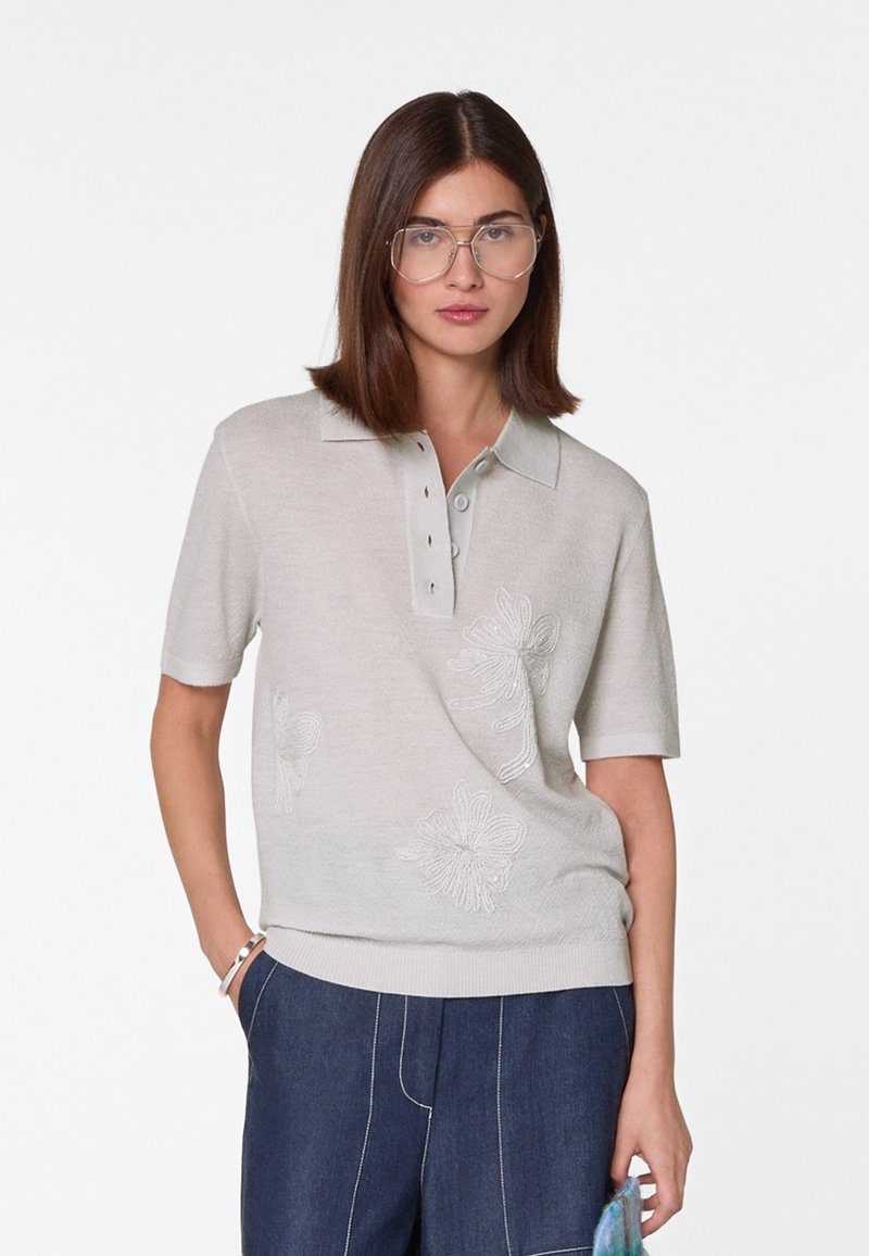 Beige polo shirt met korte mouwen van lichte stof, voorzien van bloemenborduursel op de voorkant en een drie-knopenpok met een relaxte pasvorm.