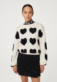 Witte gebreide trui met grote zwarte donzige hartpatronen, geribbelde manchetten, gecombineerd met een textuurrijke zwarte corduroy rok.