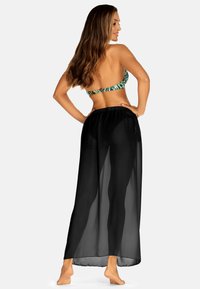 Czarna, przezroczysta spódnica maxi z elastycznym pasem, noszona na kolorowy top bikini z tropikalnym wzorem liści.