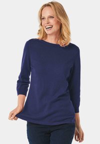 Navyblauer gestrickter Pullover, Bootsausschnitt, Dreiviertelärmel, gerippter Saum, weiche Textur, kombiniert mit dunklen Jeans, lässiger Schnitt.