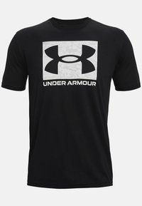 Černé tričko s krátkým rukávem s velkým bílým logem Under Armour a šedým kamuflážním pozadím uvnitř obdélníkového obrysu. Měkká, odolná tkanina.