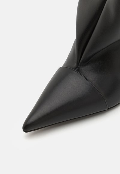 Pantofii din piele neagră cu vârf ascuțit au o textură netedă și un design pliat la gleznă. Dispun de o siluetă știrbă pentru un aspect elegant.