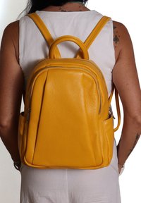 Zaino in pelle gialla, finitura strutturata, scomparti con zip, manico arrotondati, spallacci regolabili, design elegante.