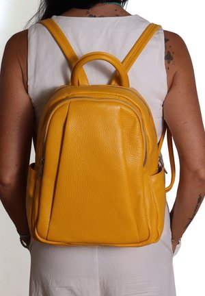 Sac à dos en cuir jaune, finition texturée, compartiments zippés, poignée supérieure arrondie, bretelles ajustables, design épuré.