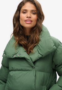 Giacca verde a vento con colletto grande, bottoni a pressione e finitura morbida e textured. Il design è trapuntato per un'ulteriore isolamento.