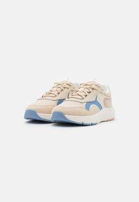 Des baskets avec un schéma de couleurs beige et bleu, présentant une texture en daim, une forme arrondie et une semelle en caoutchouc blanche avec des détails en relief.