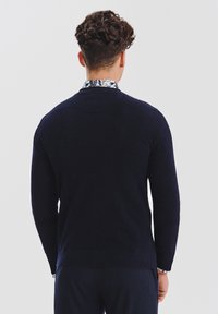 Granatowy sweter z dzianiny o teksturowanym wykończeniu, z okrągłym dekoltem i prążkowanymi mankietami, nałożony na wzorzysty kołnierz.