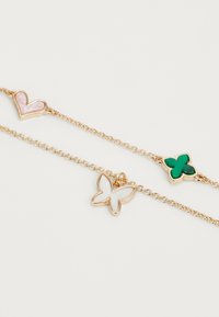 Bracciale a catena in tonalità oro con charms a forma di cuore rosa, farfalla verde e fiore verde. Accenti in smalto lucido abbelliscono le forme.