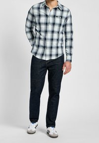 Randig knäppskjorta i ljusblått och marinblått, tillsammans med mörka denimjeans. Skorna är vita med svarta och blå accenter.