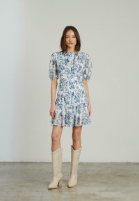 Abito floreale in azzurro chiaro e bianco, con maniche a sbuffo, vita aderente e strati di volant. Abbinato a stivali da cowboy bianchi.