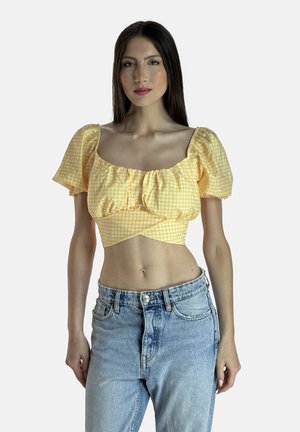 Top corto in gingham giallo con maniche a sbuffo e dettaglio arricciato, abbinato a jeans in denim azzurro chiaro a vita alta. Tessuto con una texture liscia.