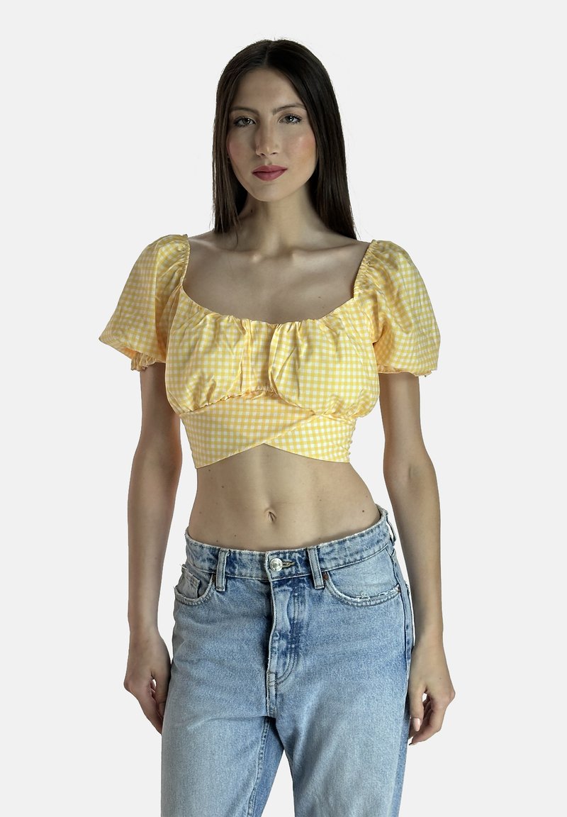 Gul rutigt crop-top med puffärmar och samlad detalj, i kombination med högmidjade ljusblå denimjeans. Slät tygtextur.