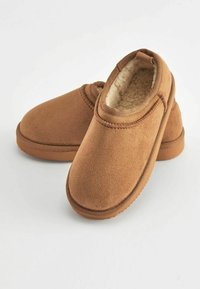 Zapatillas slip-on marrones con exterior de suave ante, forro de felpa, diseño de puntera redondeada y suela de goma texturizada para mayor agarre.