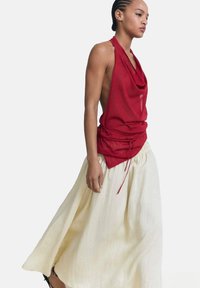 Top sin mangas rojo con escote drapeado y detalle de cordón, combinado con una falda larga blanca y fluida, hecha de tela ligera.