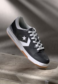 Black leather sneaker with white accents, featuring a star logo, rubber sole with gum bottom, and white laces. Simple, low-profile design.