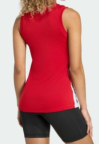 Haut de sport rouge sans manches avec une coupe ajustée, une texture douce et des accents blancs sur les côtés, associé à un short noir ajusté.