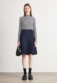 Langärmliges, gestreiftes Oberteil in Marineblau und Weiß, kombiniert mit einem Marineblauen A-Linien-Rock. Schwarze Plateauschuhe und eine schwarze Handtasche runden den Look ab.