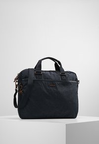 Mørkegrå stofpose med robuste håndtag, justerbar skulderrem, lynlåslomme foran og bronzefarvede hardware-detajler. Har brandlogo på forsiden.