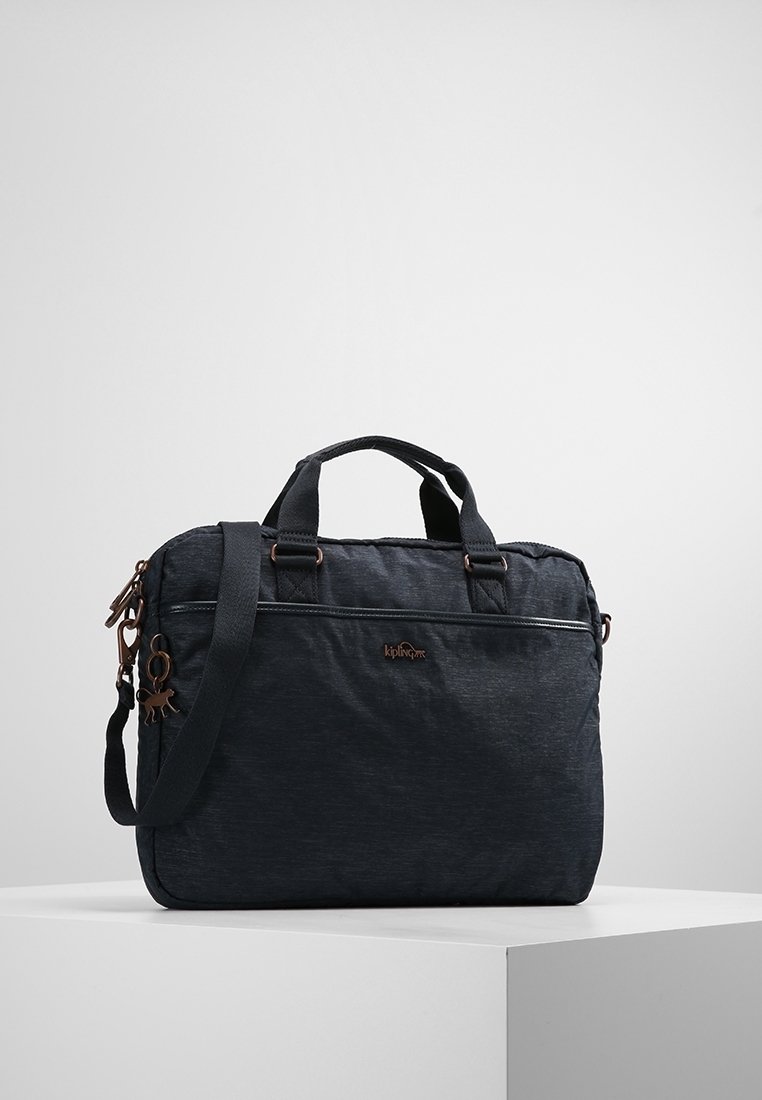 Mørkegrå stofpose med robuste håndtag, justerbar skulderrem, lynlåslomme foran og bronzefarvede hardware-detajler. Har brandlogo på forsiden.