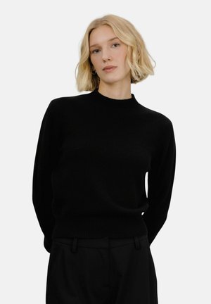 Svart strikkegenser med rund hals, lange ermer og en tettsittende midje. Jevn tekstur uten synlige mønstre eller detaljer.