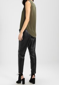 Top sans manches vert olive associé à un pantalon en cuir noir fuselé et des bottines à talons carrés noires ; tissu lisse et coupe décontractée.
