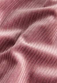 Tessuto di velluto rosa a coste con una texture morbida, caratterizzato da un leggero lucido e linee verticali uniformi. Il materiale appare soffice e lussuoso.