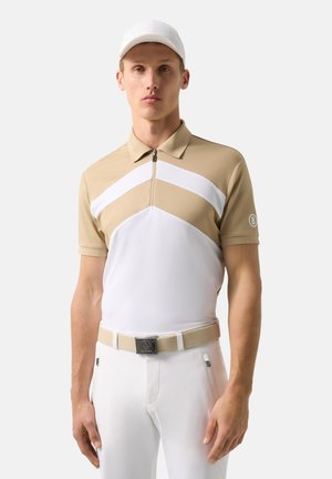 Young man wearing beige and white short-sleeve polo with zipper, white cap, white pants, and beige belt, standing against a plain background.