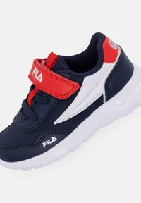 Scarpa sportiva blu navy con dettagli bianchi e rossi, superiore in sintetico testurizzato, strap in Velcro e suola in gomma bianca imbottita.