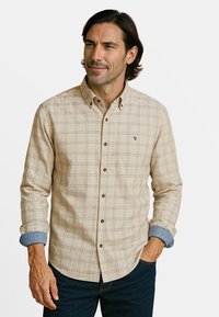 Beige geruite blouse met lange mouwen, bruine knopen en denim-achtige manchetten. Heeft een klein blauw logo op de borst.