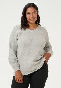Light gray sweater made of soft, textured fabric. Features a round neckline and long sleeves, paired with black pants. Simple, neutral design.