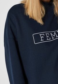 Felpa blu navy con vestibilità rilassata e scollatura rotonda. Presenta una stampa rettangolare bianca con la parola "FEM" in lettere in grassetto.