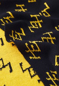 Strickstoffschal mit einem auffälligen Schwarz-Gelb-Muster. Die gelbe Seite hat eine strukturierte Oberfläche, während die schwarze Seite filigrane Designs zeigt.