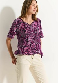 Korte mouwen top met een paars en roze abstract bladpatroon, voorzien van een V-hals en een relaxte pasvorm. Gecombineerd met lichte broeken.