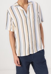 Chemise légère à manches courtes avec des rayures verticales beige, bleu clair et noir. Comprend une poche et une fermeture à boutons.