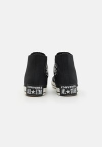 Zapatillas altas de lona negra con un parche redondo de logo y "CONVERSE ALL STAR" impreso en el talón. Suela de goma con rayas.