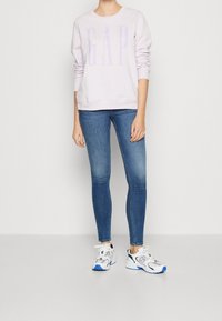 Sudadera de lavanda clara con el logo "GAP", combinada con vaqueros ajustados de mezclilla azul y zapatillas blancas con acentos en azul y verde.