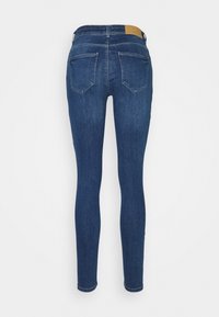 Jeans ajustados de denim azul oscuro, con una cintura alta, cinco bolsillos y una etiqueta de cuero marrón en la cinturilla trasera. Textura suave.