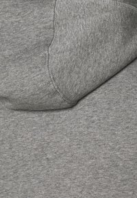 Tela de sudadera gris con una textura suave, que cuenta con una capucha y detalles de costura visibles. Apariencia ligeramente jaspeada.
