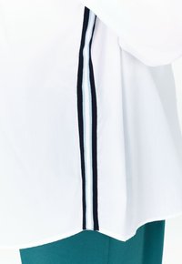 Camisa blanca con una franja navy y acentos en azul claro en el costado. La camisa tiene un dobladillo redondeado y una textura suave.