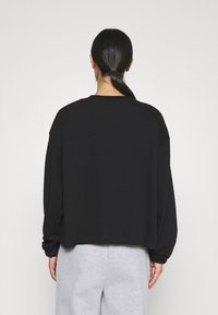 Černá, nadměrná mikina s kulatým výstřihem a dlouhými rukávy, s krátkým střihem. Hladká textura, minimální detaily.