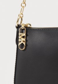 Borsa a tracolla in pelle nera con hardware in tonalità oro e dettaglio del logo firmato. Presenta una tracolla a catena e chiusura a zip nella parte superiore.