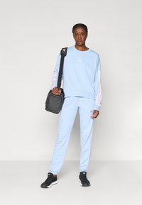 Svetlomodrá mikina s ružovými akcentmi a logom Adidas, v kombinácii s nohavicami na voľný čas v rovnakom odtieni. Čierne športové topánky a šedá ramenná taška.