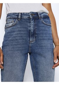 Jeans in denim blu a vita alta con un lavaggio leggermente sbiadito. Presentano cinque tasche, una chiusura con bottone e cuciture arancioni a contrasto.