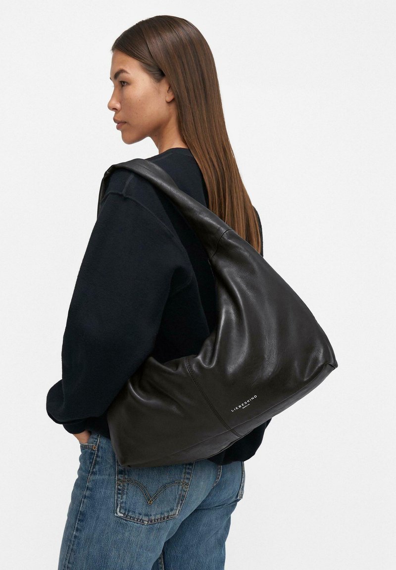 Borsa hobo in pelle nera con una forma morbida e curva e una texture liscia. Presenta un branding discreto sul lato. Indossata a spalla.