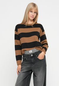 Brown and black striped knit sweater with a relaxed fit, paired with high-waisted gray denim jeans. Textured fabric and casual design.