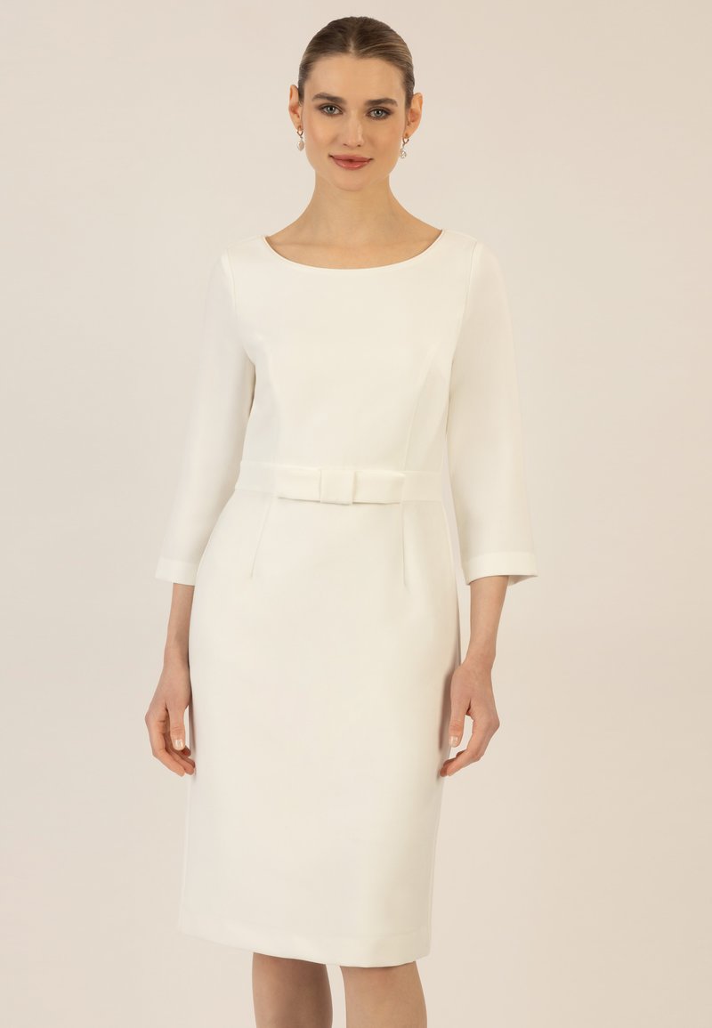 Weißes Kleid mit drei Viertelärmeln, taillierter Silhouette, Rundhalsausschnitt, Gürtel in der Taille und zwei Fronttaschen. Glatte Stofftextur.